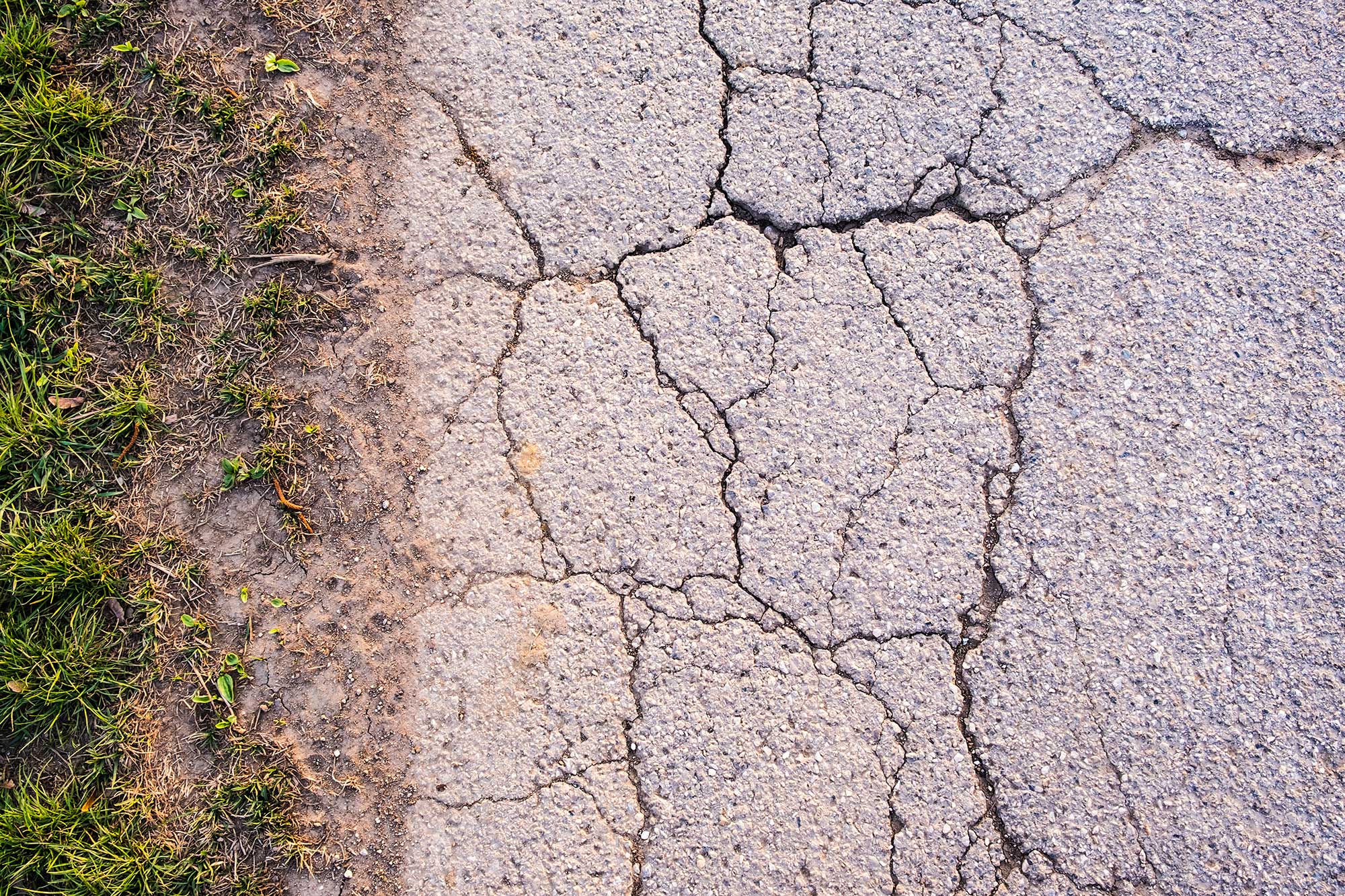 A cracked and damaged sidewalk, exhibiting surface wear that requires repair.