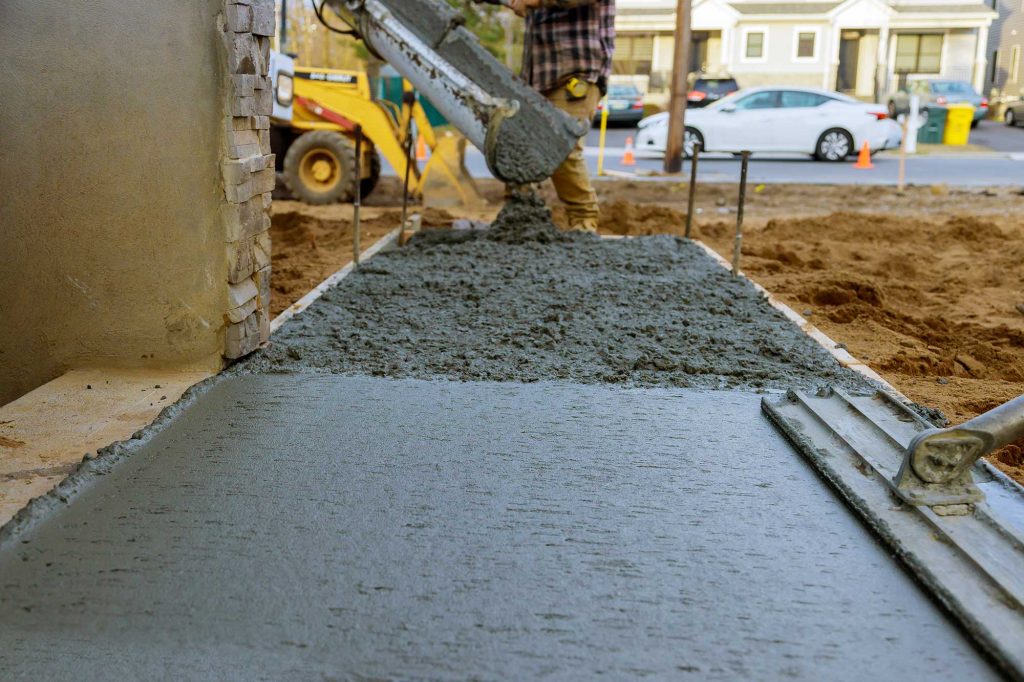 Concrete is being poured onto a construction site, with machinery and vehicles visible in the background. The scene captures the process of laying a concrete slab.